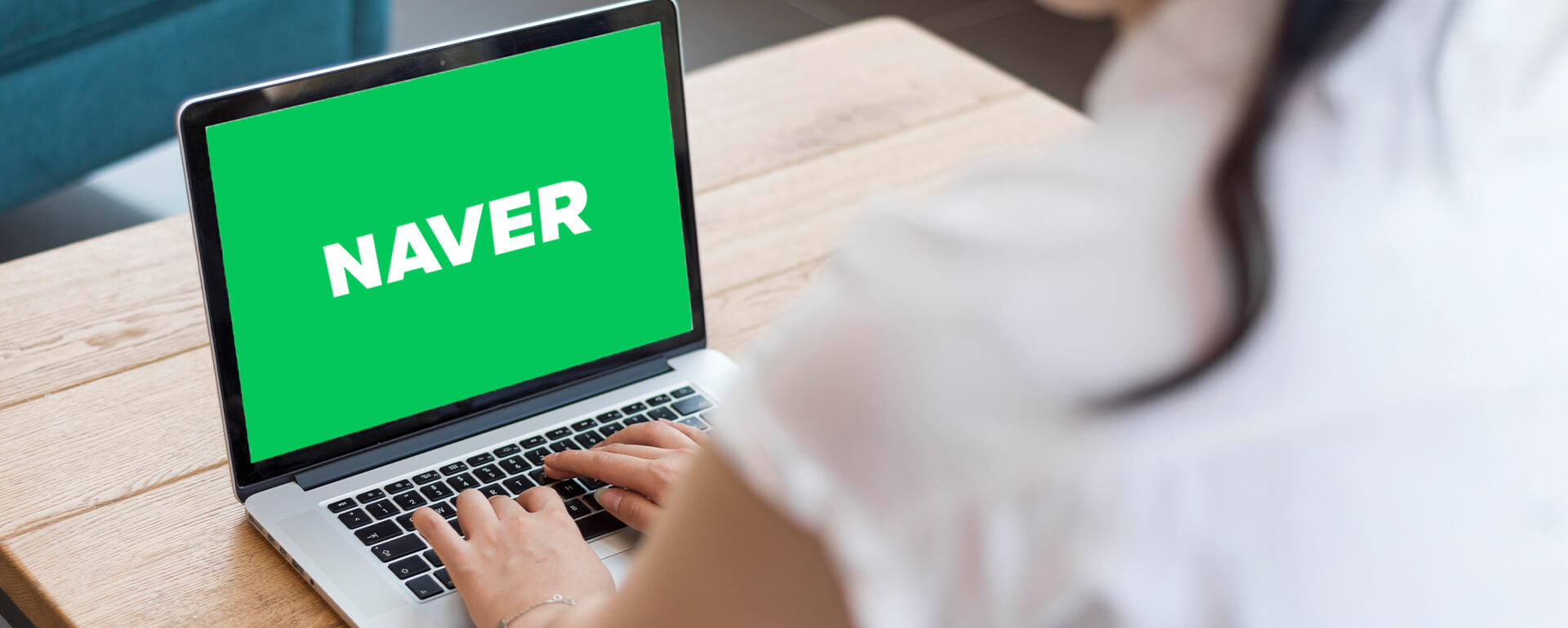 Person tippt auf einem Laptop mit grünem Bildschirm und weißem Schriftzug 'NAVER' auf einem Holztisch