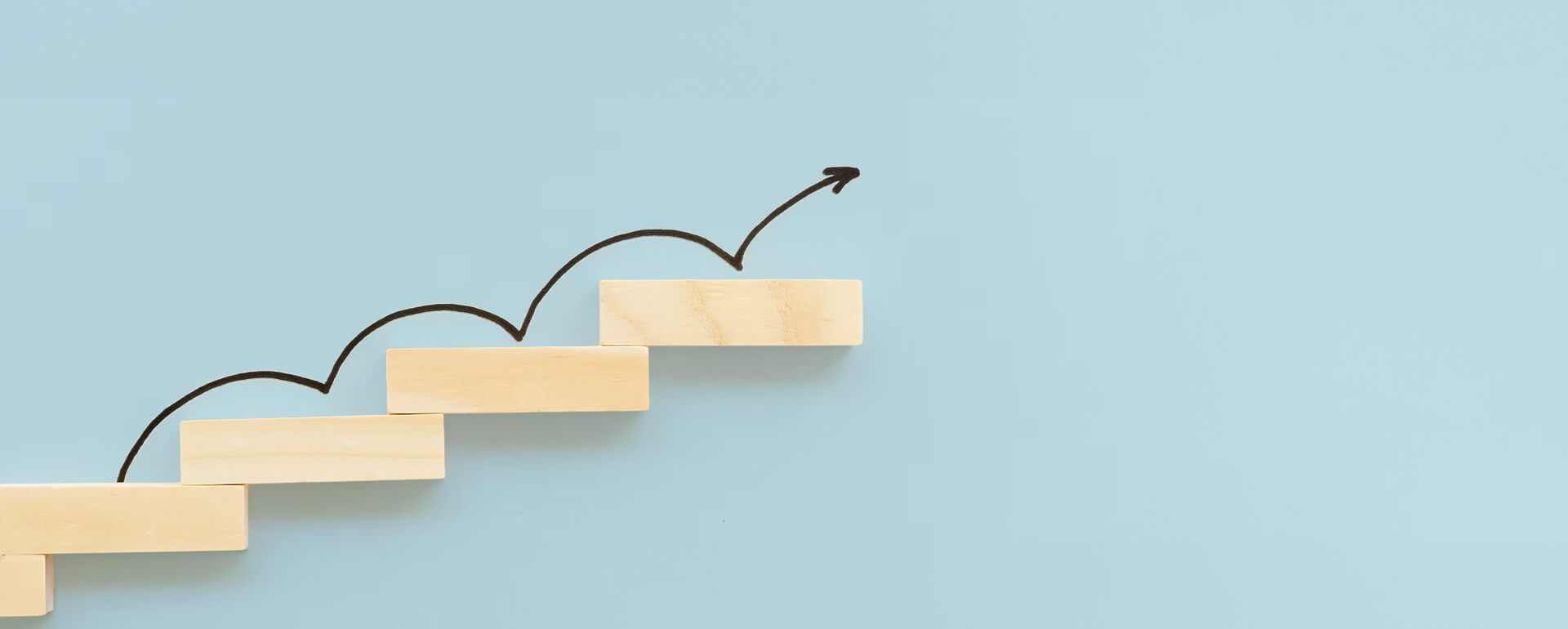 Holzstufen mit aufsteigendem Pfeil vor hellblauem Hintergrund