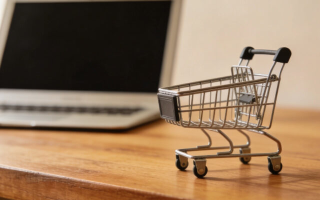 Kleiner Einkaufswagen auf einem Holztisch vor einem geöffneten Laptop