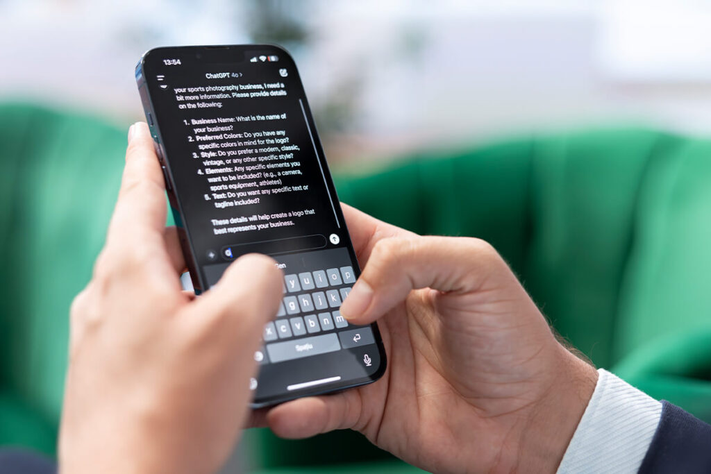 Hände halten ein Smartphone mit einer ChatGPT-Antwort auf dem Bildschirm und einer sichtbaren Tastatur